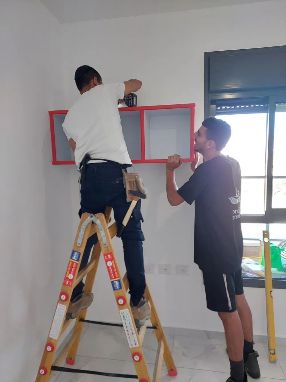 צוות ג'אמפ הובלות מרכיב מדף על הקיר